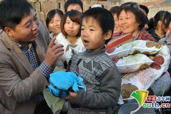 2013年冬天,路仲良(左一)为村里留守儿童筹建了爱心书屋。图为捐赠现场,路仲良在教6岁留守儿童路亚衡向来村的社会爱心人士道谢。 路仲良供图